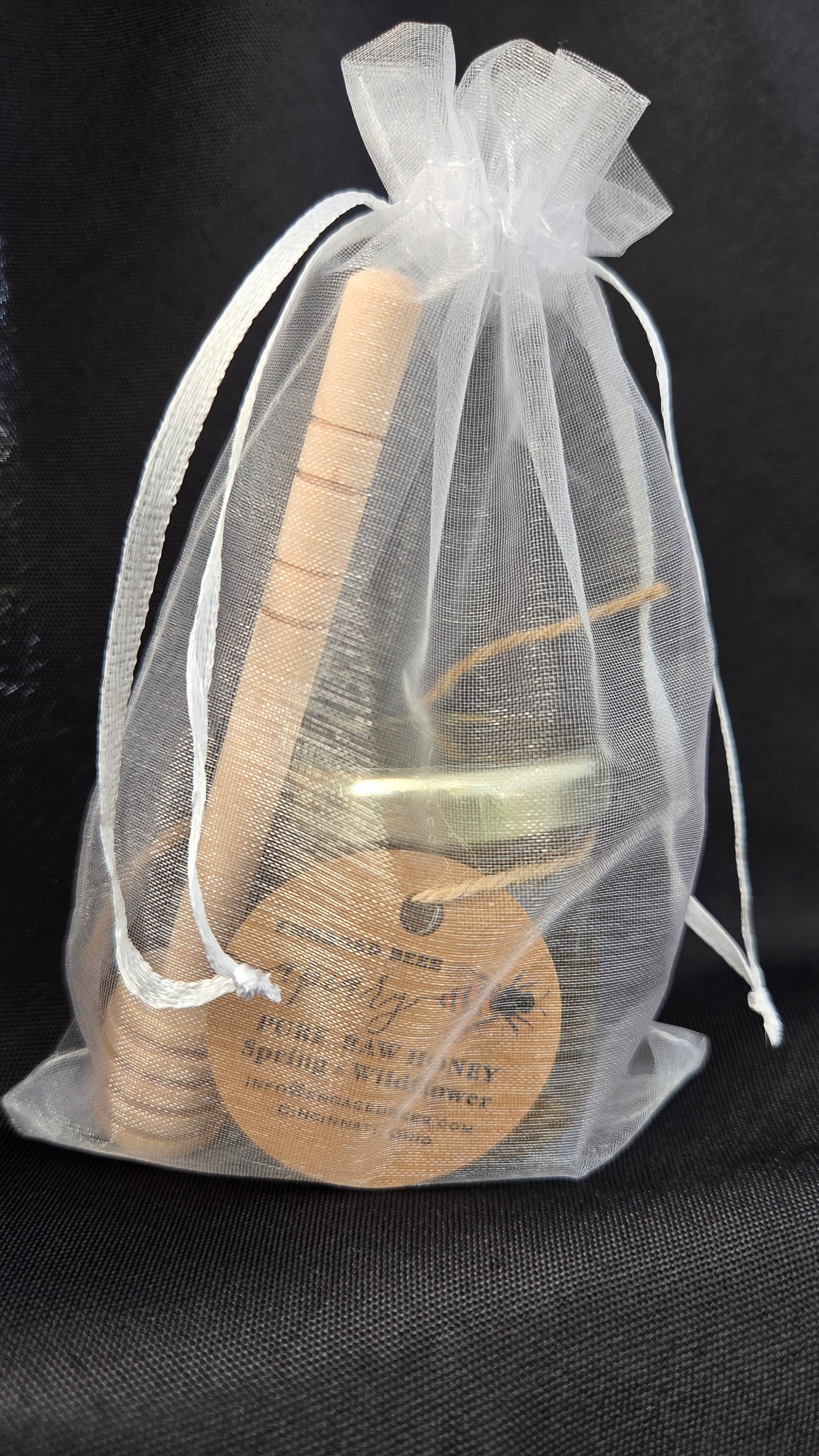 Small cylinder bottle of spring honey with a honey dipper in an organza bag